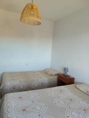 A bedroom with two beds, a bedside table with a lamp, and a hanging light fixture.
