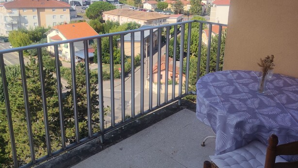 Varanda com mesa e cadeira, vista para área residencial com casas e montanhas ao longe.