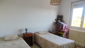 Quarto com duas camas de solteiro, mesa de cabeceira com abajur, cômoda e janela com persianas.