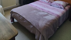 Quarto com cama, radiador, janela com cortinas e luminária suspensa.