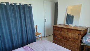 Quarto com cama, cómoda de madeira, cadeira, espelho e porta.