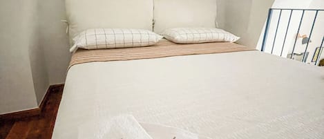Un dormitorio con cama, almohadas, una toalla y una mesita de noche con lámpara.