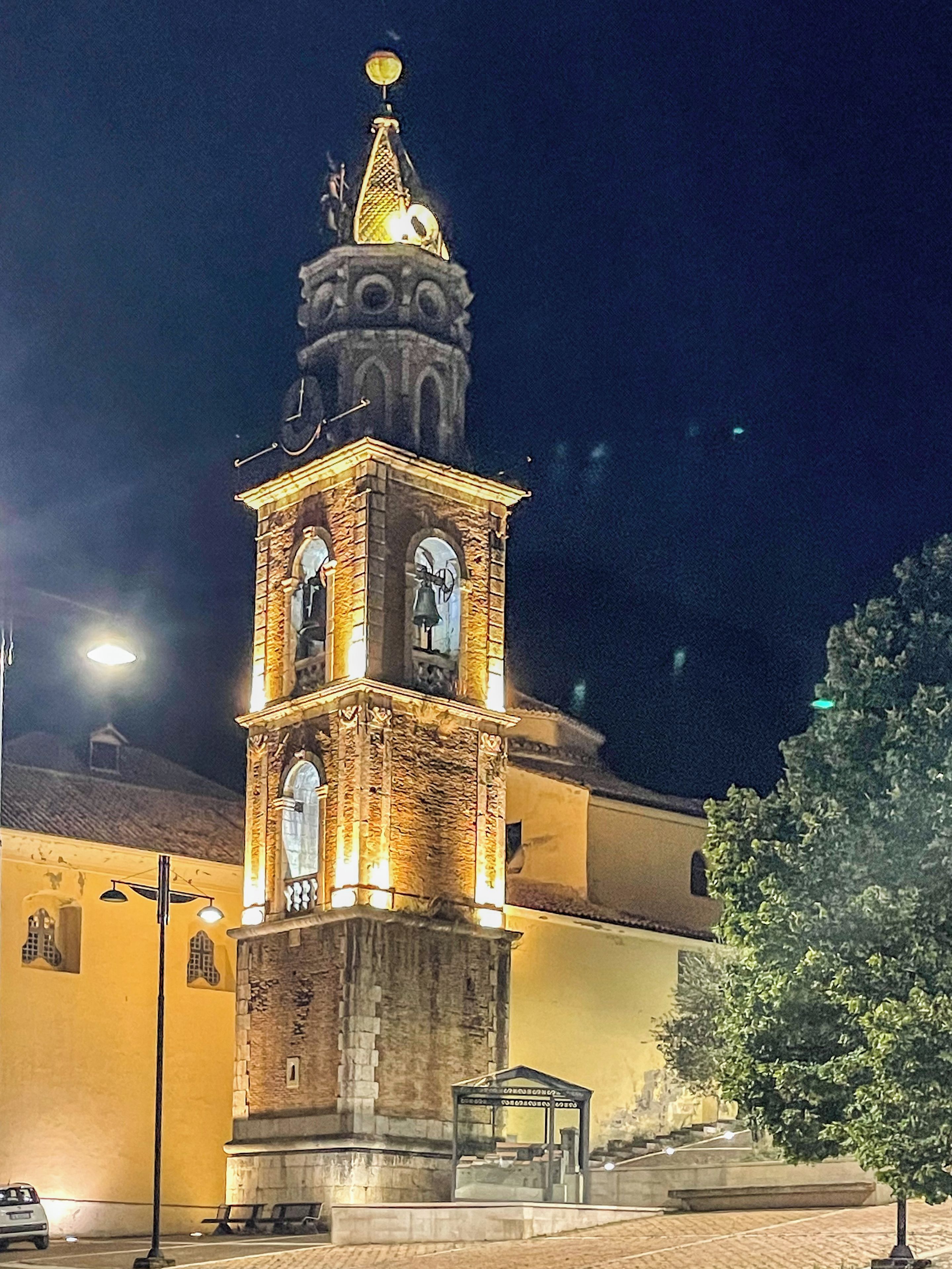 A historic building with a prominent clock tower, a bell, and a small shelter.