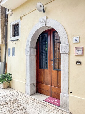Une entrée d’immeuble avec une porte en bois, un portail en arc de cercle, une boîte aux lettres et une petite plante en pot.