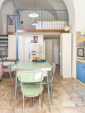 A dining area with a table and chairs, a refrigerator, a clock, and a staircase leading to an upper level. - Il Mandorlo di Pierina (Vitulano)