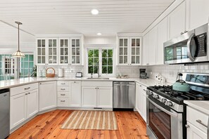 A modern kitchen with white cabinetry, a stainless steel dishwasher, a gas stove, and a microwave. - Lakeside Charmer Steps To Association Beach! (Lakeside)
