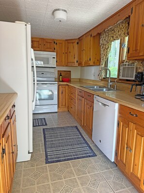 A compact kitchen with wooden cabinets, a white refrigerator, a microwave, a stove, a sink, and a dishwasher.