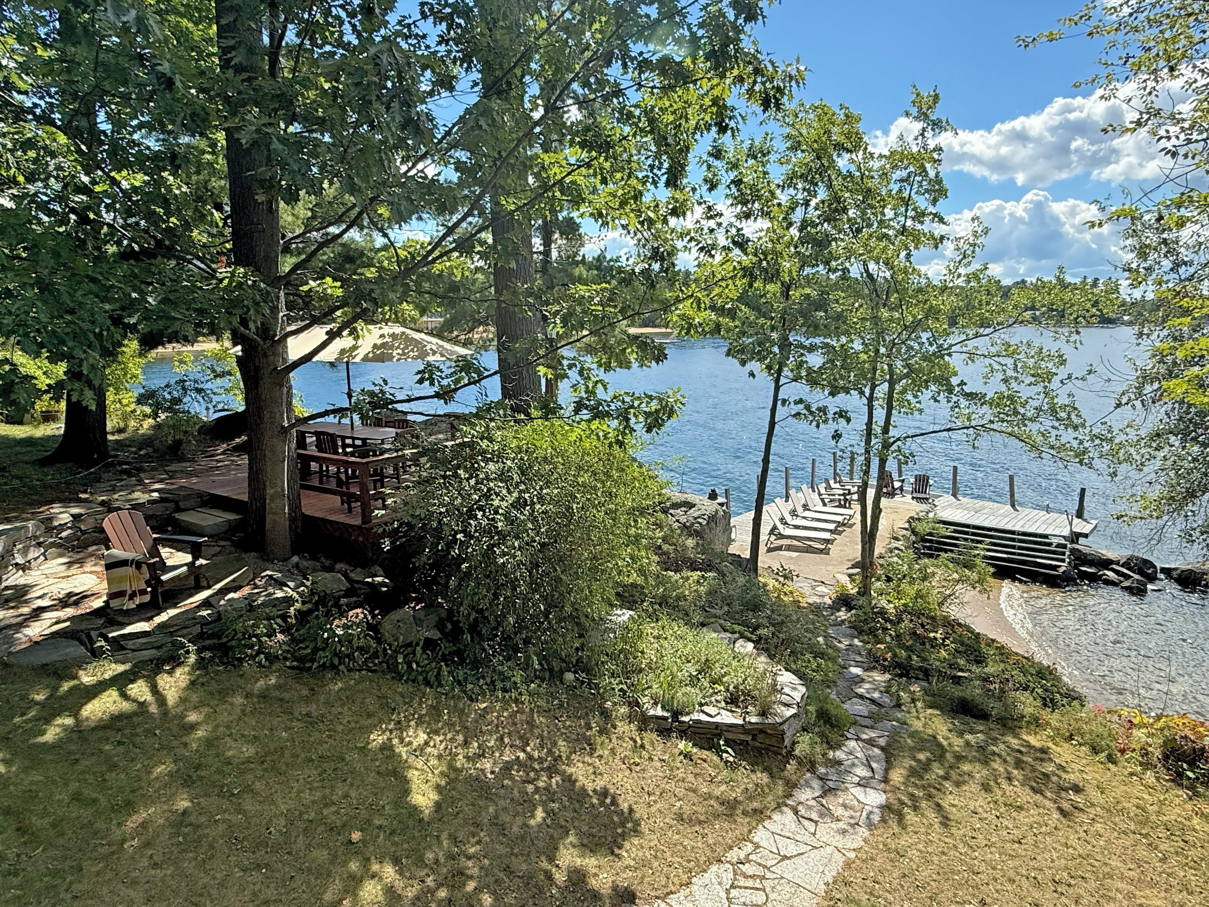 A lakeside deck with outdoor seating and a stone pathway leading to a dock.