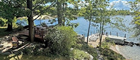 A lakeside deck with outdoor seating and a stone pathway leading to a dock.