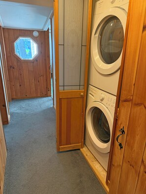 A laundry room with a washing machine and dryer, wooden walls, a small window, and a door.