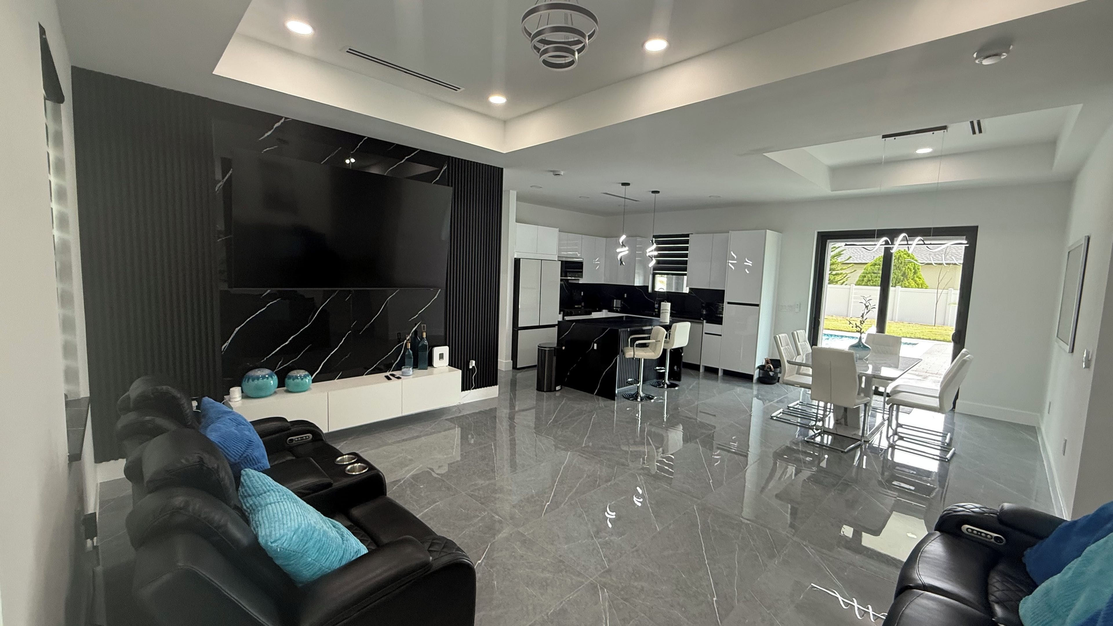Una sala moderna con un sofá de cuero negro, un televisor de pantalla plana y una cocina con armarios blancos y una encimera negra.