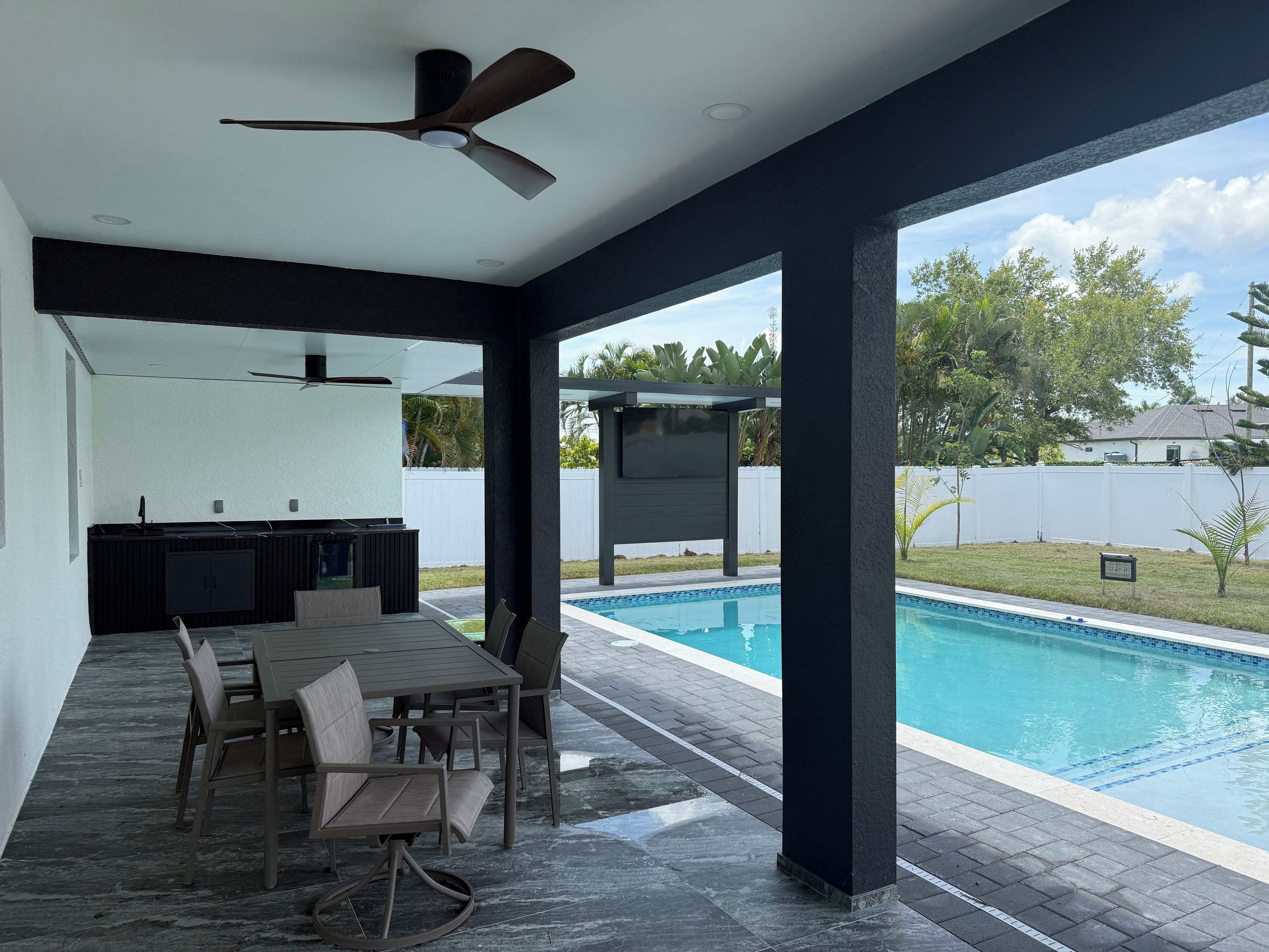Un espacio exterior techado con piscina, una mesa de comedor con sillas y un ventilador de techo.