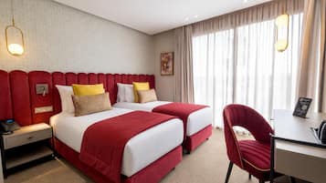 A hotel room with two beds, a desk, a chair, and a large window with curtains.