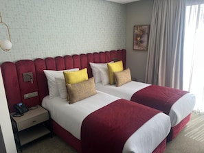 Een hotelkamer met twee bedden, een nachtkastje met een telefoon en een raam met gordijnen.