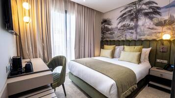Habitació d'hotel amb llit, escriptori, cadira, tauleta de nit i televisió penjada a la paret.