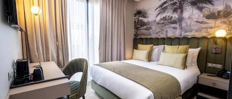 Habitación de hotel con cama, escritorio, silla, mesita de noche y televisor de pared.