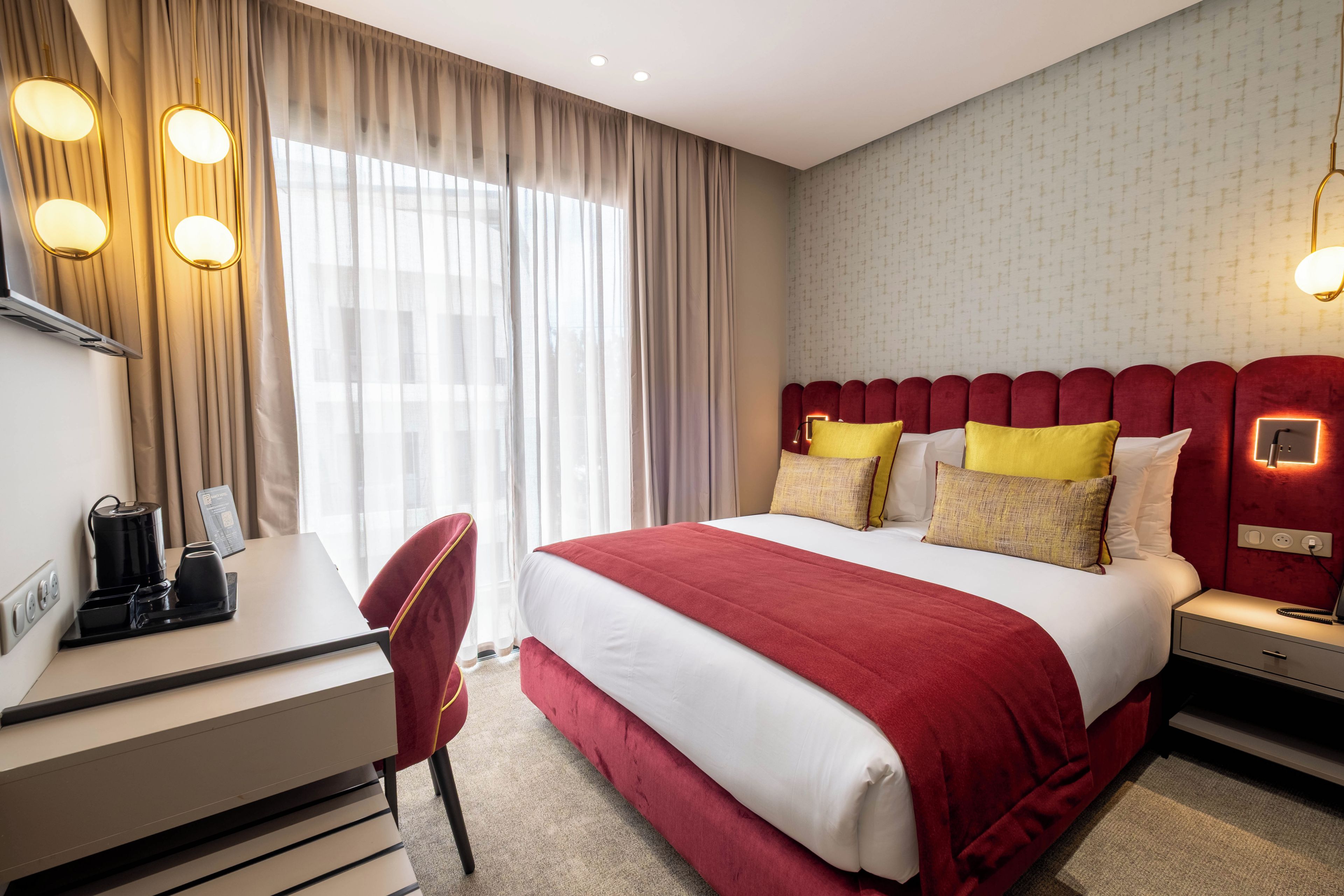 A hotel room with a bed, bedside tables, a desk, a chair, and a window with curtains.