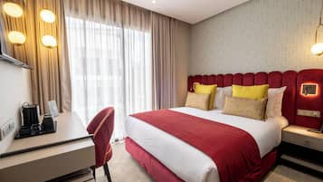 A hotel room with a bed, bedside tables, a desk, a chair, and a window with curtains.