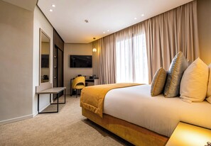 A hotel room with a large bed, a desk, a chair, a flat-screen TV, and a mirror.