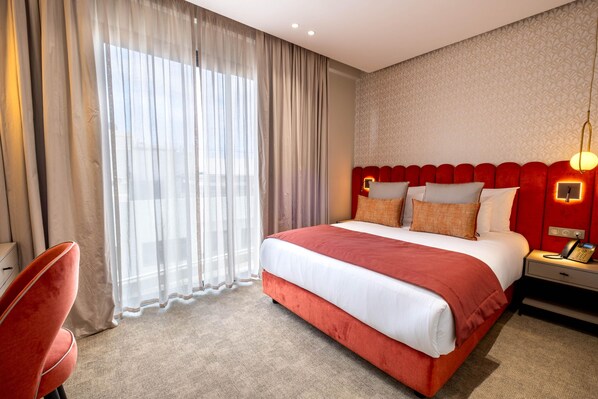 A hotel room with a large bed, a desk with a phone, and a chair.