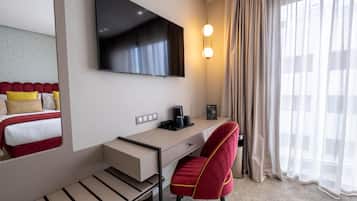 A hotel room with a bed, a desk, a chair, a TV, a coffee maker, and a window with curtains.
