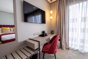 A hotel room with a bed, a desk, a chair, a TV, a coffee maker, and a window with curtains.