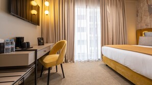 A hotel room with a bed, a desk, a chair, a coffee maker, and a minibar.
