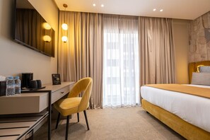 A hotel room with a bed, a desk, a chair, a coffee maker, and a minibar.