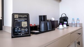 A hotel room with a self-service kiosk, coffee maker, water bottles, and a trash bin.