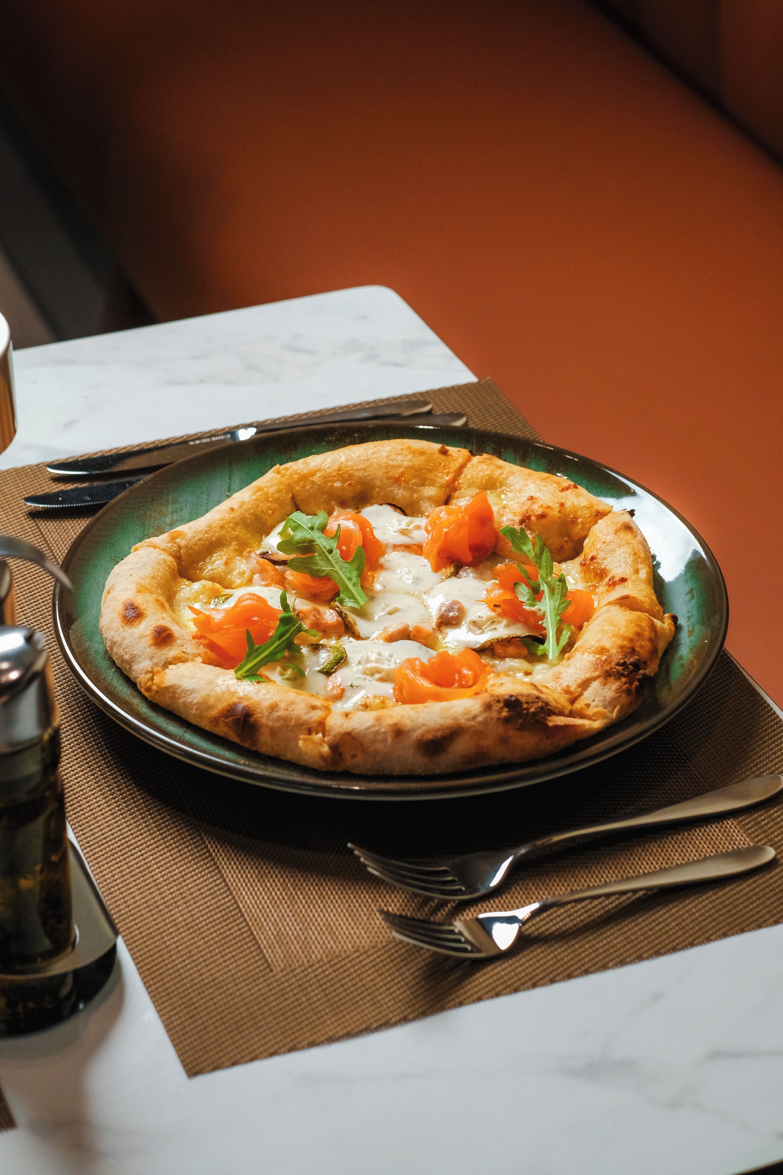 Una pizza sobre un plato verde, con un tenedor y un cuchillo a un lado.