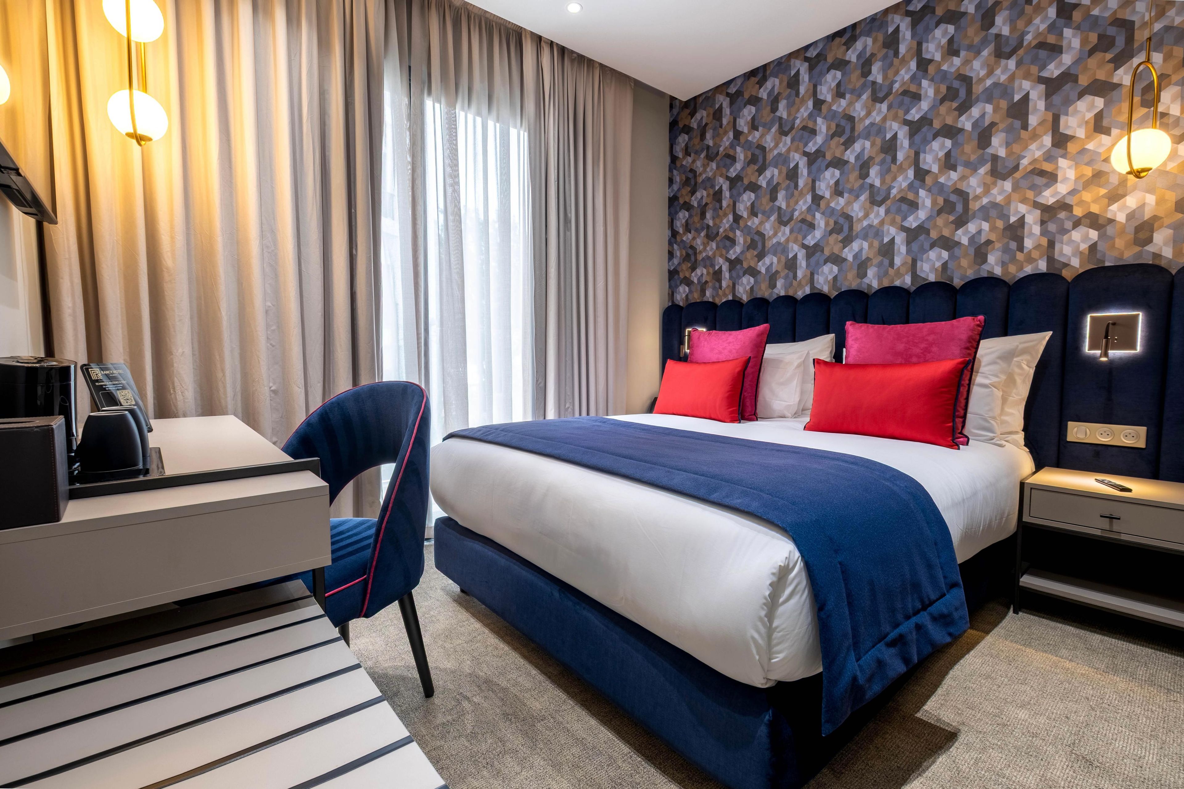A hotel room with a bed, bedside table, chair, and a desk with a telephone.