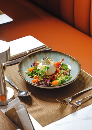 A plate of food with a poached egg on top, surrounded by greens and vegetables, placed on a textured placemat.