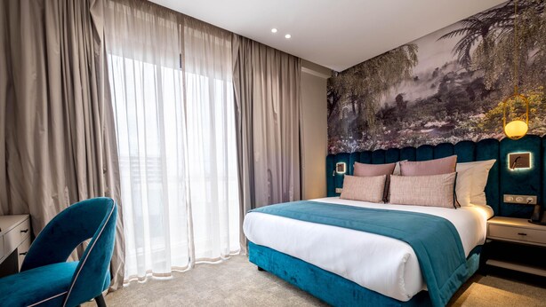 A hotel room with a large bed, a desk, a chair, and a mural on the wall.