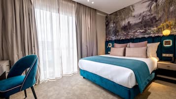 Quarto de hotel com uma cama grande, uma escrivaninha, uma cadeira e um mural na parede.