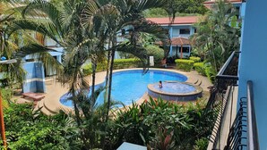 A pool area with a hot tub, surrounded by palm trees and a building with a red-tiled roof. - Marina Loft Unit 224,2 Floor (Sardinal)