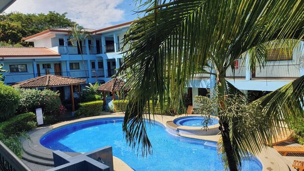 A pool area with a hot tub, surrounded by palm trees and a building with a tiled roof. - Marina Loft Unit 224,2 Floor (Sardinal)