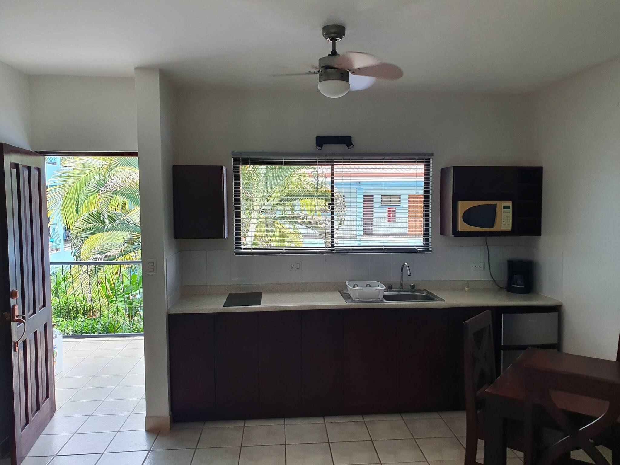 A compact kitchen with a window, a ceiling fan, and a microwave.