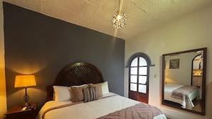 Een slaapkamer met een groot bed, een nachtkastje, een lamp, een spiegel en een raam met uitzicht op het interieur.