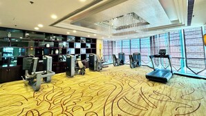 A hotel gym with exercise equipment, a patterned carpet, and large windows. - Chongqing Empark Grand Hotel (Chongqing)