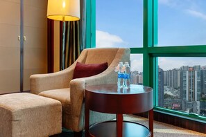 A hotel room with a large window, a sofa, a small table with a water bottle, and a lamp. - Chongqing Empark Grand Hotel (Chongqing)