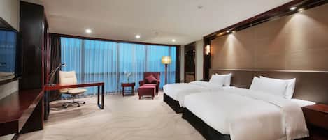 Une chambre d’hôtel avec un grand lit, un bureau, une chaise et une vue sur l’extérieur grâce à de grandes fenêtres.