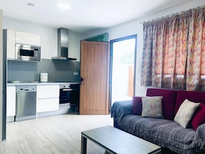 A modern kitchen with a microwave, oven, and dishwasher. There is a wooden door leading to a balcony. A sofa with patterned cushions is in the living area. - Apartment La Solanita for Relaxing Retreat (Artenara)