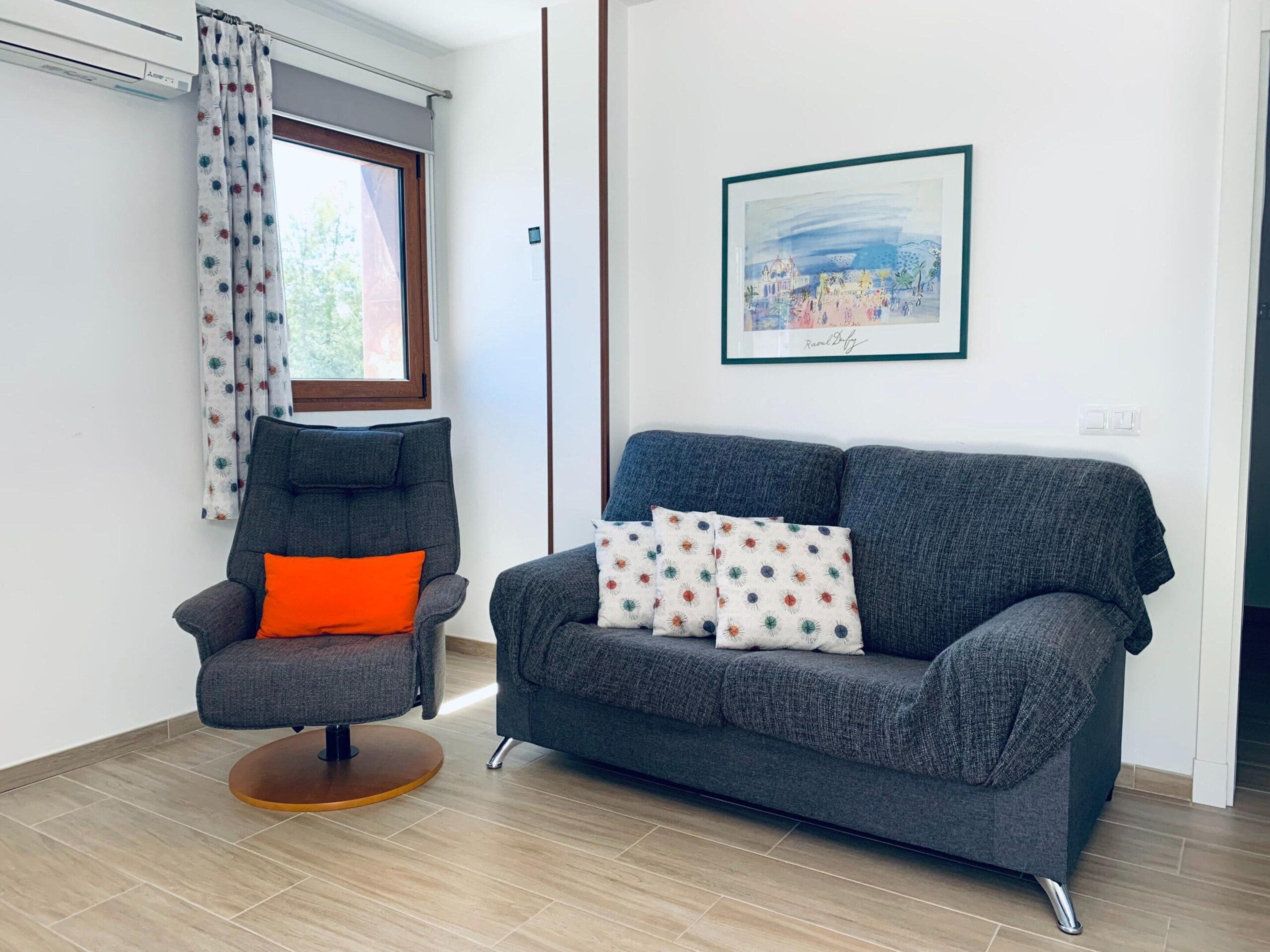 Ein Wohnzimmer mit einem grauen Sessel, einem grauen Sofa und einem gerahmten Bild an der Wand.