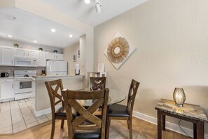 A modern kitchen with white appliances and a dining area with wooden chairs and a glass table. - Near Disney! 3BR Kissimmee Townhome, Pools & Spa (Kissimmee)