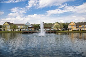 A row of houses with a central fountain, a calm lake, and a clear sky. - Near Disney! 3BR Kissimmee Townhome, Pools & Spa (Kissimmee)