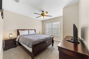A bedroom with a bed, bedside table, lamp, window with blinds, ceiling fan, and a desk with a television. - Near Disney! 3BR Kissimmee Townhome, Pools & Spa (Kissimmee)