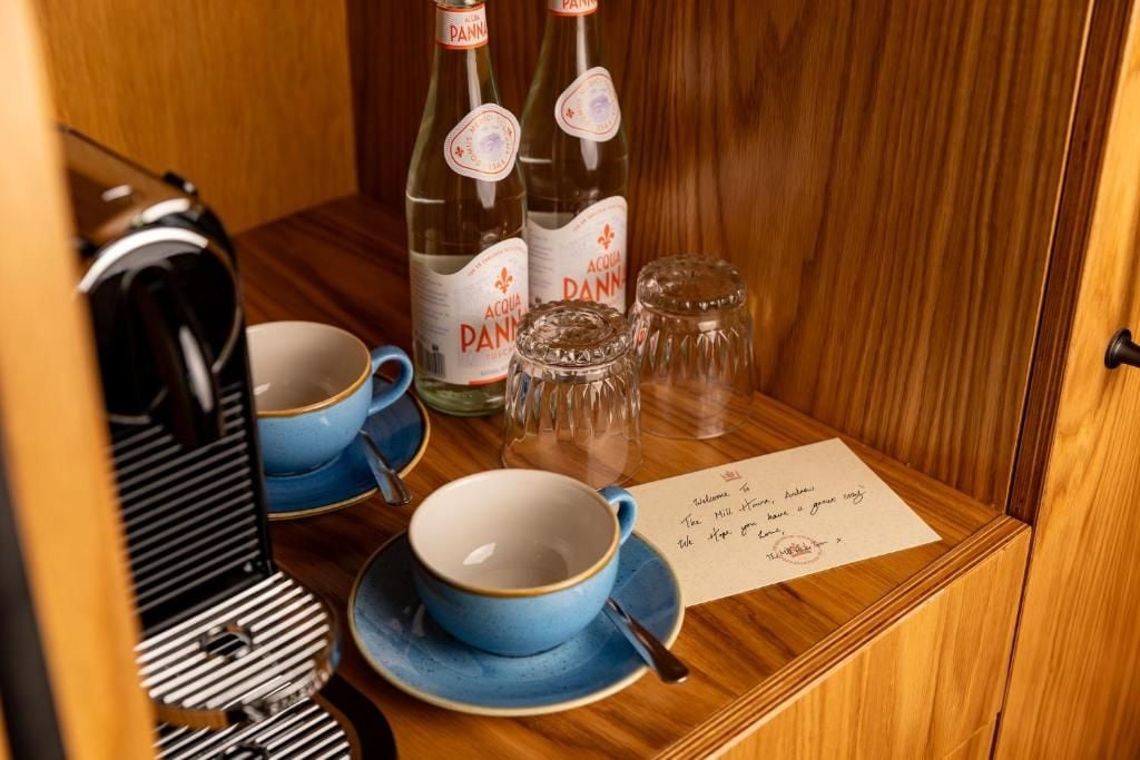 Una mesa de madera con dos botellas de Acqua Panna, dos tazas azules, una cuchara y una nota escrita a mano.
