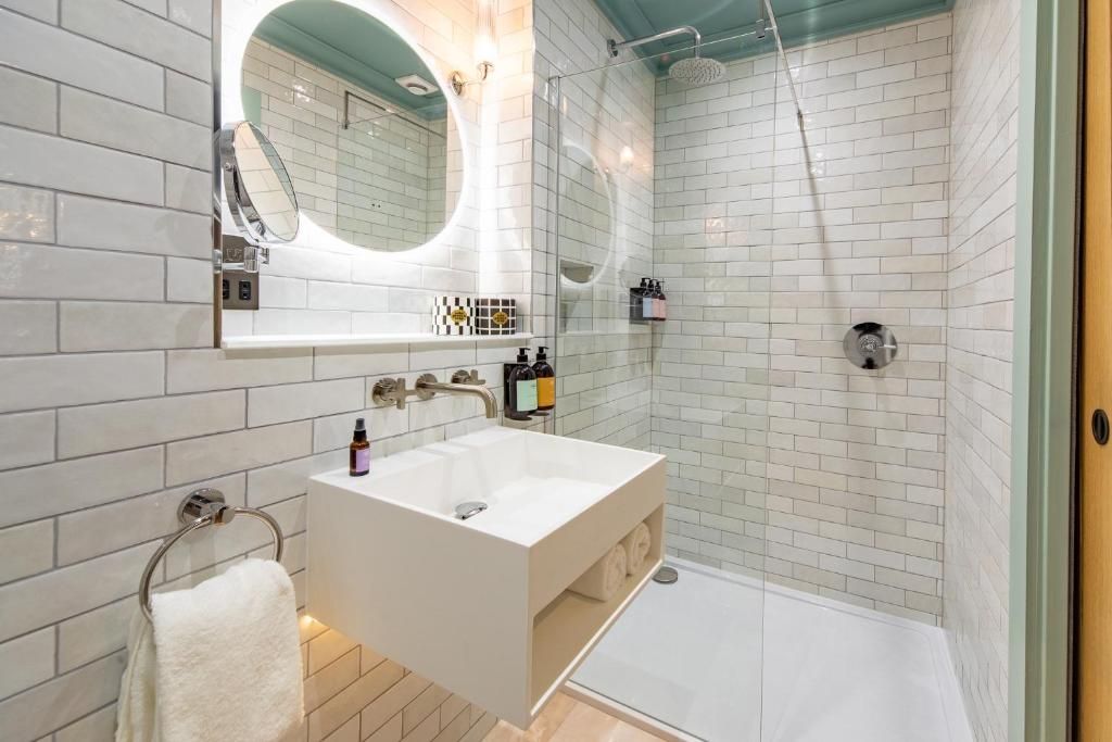 Un baño moderno con un lavamanos blanco, un espejo y una ducha con mampara de vidrio.