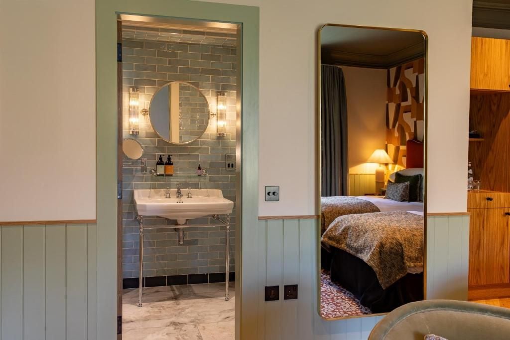 A bathroom with a sink, mirror, and a view into a bedroom with a bed and nightstand.