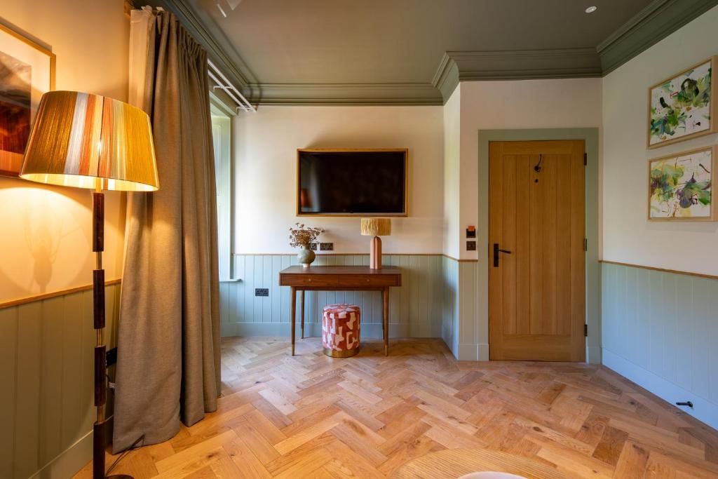 Een kamer met een visgraatvloer, een houten deur, een tafel met een vaas en een lamp.